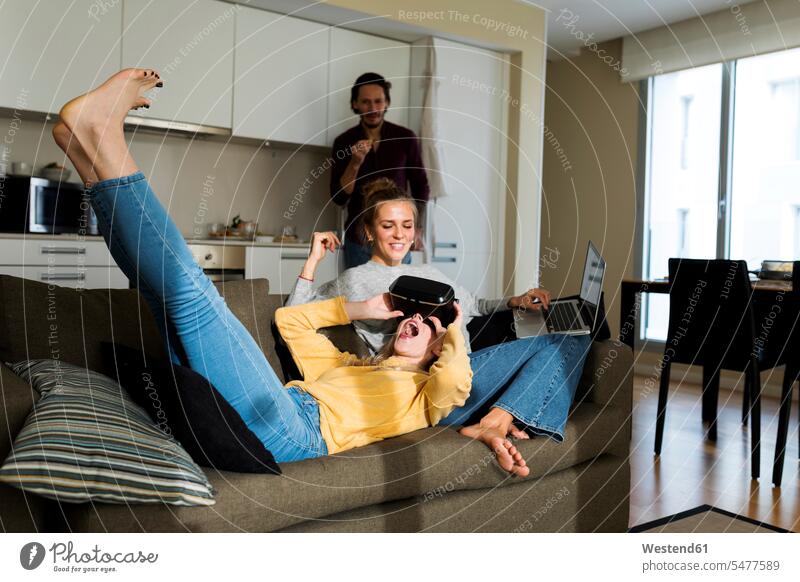 Freunde sitzen auf der Couch im Wohnzimmer und spielen mit einer VR-Brille liegen liegend liegt Zuhause zu Hause daheim Gemeinsam Zusammen Miteinander Wohnraum