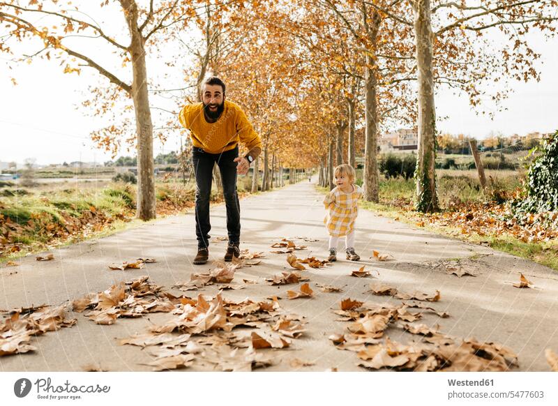 Vater und Tochter spielen auf einem Weg im Park im Herbst Blatt Blaetter Blätter starten Papas Väter Vati Vatis Papis Töchter Freude freuen morgens Morgen früh