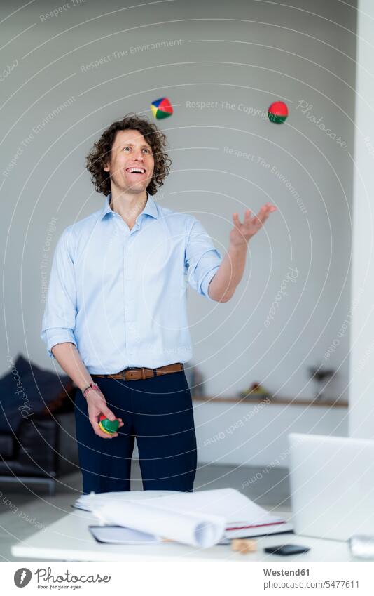 Lachender Geschäftsmann jongliert in seinem Büro mit Bällen Ball spielen glücklich Glück glücklich sein glücklichsein jonglieren Office Büros lachen