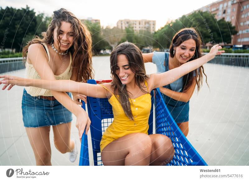 Drei verspielte Freundinnen mit Einkaufswagen in der Stadt Freunde Kameradschaft dunkle Haare braunes Haar braunhaarig brünett Warenkorb Jahreszeiten sommerlich
