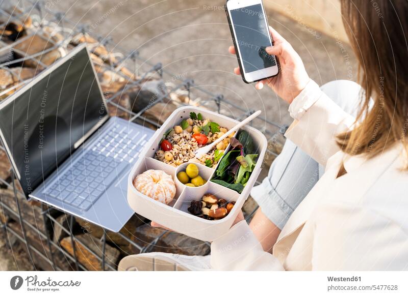 Unternehmerin benutzt Smartphone mit wiederverwendbarer Lunchbox Farbaufnahme Farbe Farbfoto Farbphoto Außenaufnahme außen draußen im Freien Tag