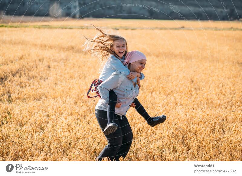 Eine krebskranke Frau, die ihre Tochter auf dem Rücken trägt, lachend Leute Menschen People Person Personen Europäisch Kaukasier kaukasisch 2 2 Menschen