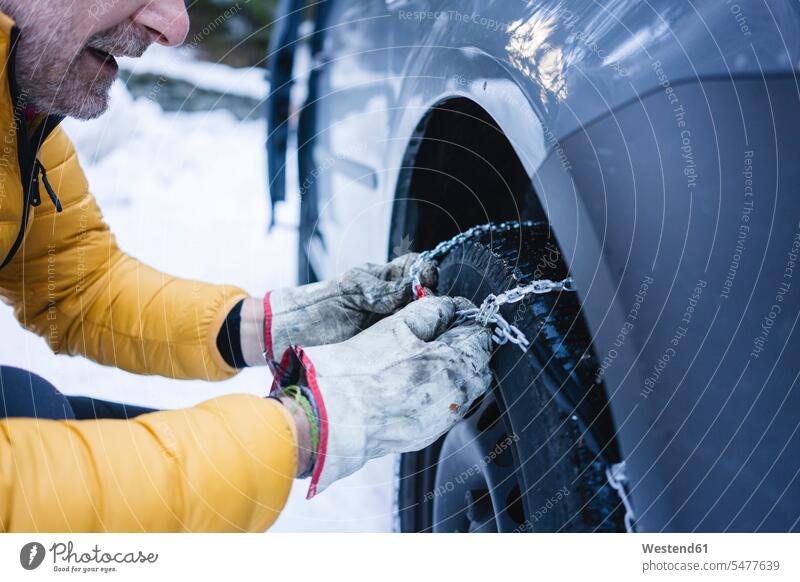 Mann legt die Schneeketten an sein Auto Handschuhe Jacken Automobil Autos PKW PKWs Wagen Jahreszeiten winterlich Winterzeit Kälte geschützt schützen Absicherung