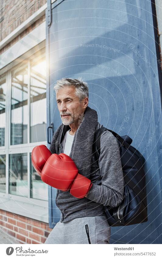 Porträt eines reifen Mannes mit Handtuch, Sporttasche und roten Boxhandschuhen vor einer Turnhalle stehend Handtuecher Handtücher Portrait Porträts Portraits