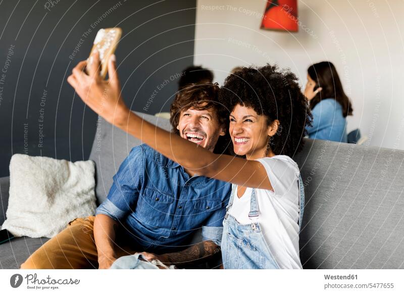Glückliches Paar sitzt auf der Couch und macht ein Selfie glücklich glücklich sein glücklichsein Sofa Couches Liege Sofas Selfies Pärchen Paare Partnerschaft
