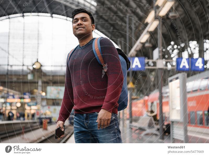 Mann mit Smartphone, der am Bahnhof auf den Zug wartet Touristen Rucksäcke Telekommunikation telefonieren Handies Handys Mobiltelefon Mobiltelefone freuen
