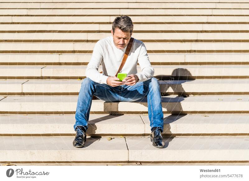 Lässiger Geschäftsmann, der auf einer Treppe sitzt und Nachrichten auf seinem Smartphone liest Businessmann Businessmänner Geschäftsmänner reifer Mann