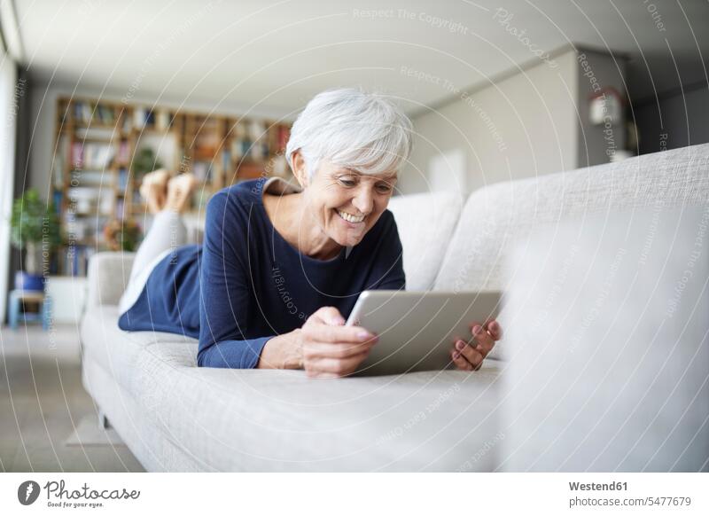 Ältere Frau mit digitalem Tablett zu Hause auf dem Sofa liegend Farbaufnahme Farbe Farbfoto Farbphoto Innenaufnahme Innenaufnahmen innen drinnen Tag