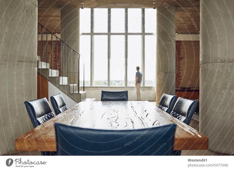 Holztisch in einer Dachgeschosswohnung mit einem Mann am Fenster im Hintergrund Stuehle Stühle Tische Holztische stehend steht Innenarchitektur Muße Individuell