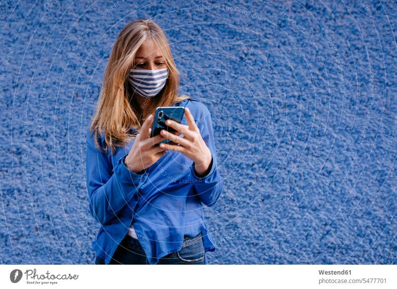 Junge Frau mit Maske und Smartphone, die in der Stadt an der Wand steht Farbaufnahme Farbe Farbfoto Farbphoto Spanien Freizeitbeschäftigung Muße Zeit Zeit haben
