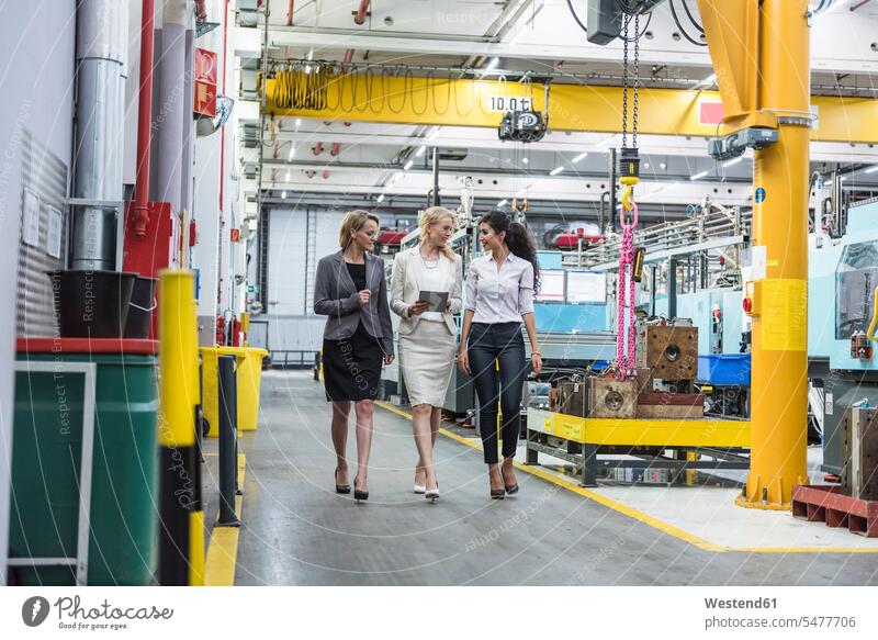 Drei Frauen mit Tablette zu Fuß und im Gespräch in der Fabrik Fabrikhalle sprechen reden Industriehallen Fabrikhallen weiblich Tablet Computer Tablet-PC