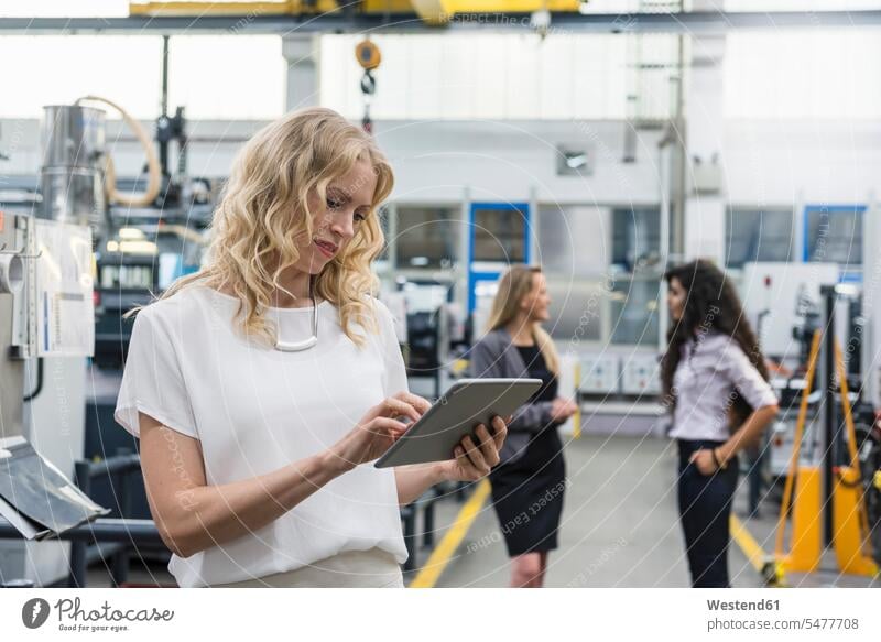Frau mit Tablet in Fabrikhalle mit zwei Frauen im Hintergrund Fabriken Industriehallen Fabrikhallen weiblich Tablet Computer Tablet-PC Tablet PC iPad