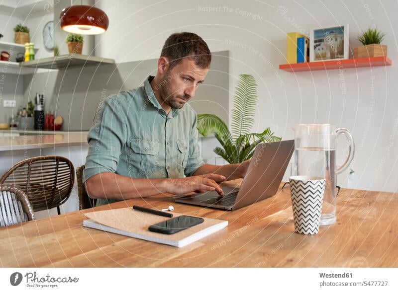 Gut aussehender männlicher Freiberufler mit Laptop am Esstisch, während er von zu Hause aus arbeitet Farbaufnahme Farbe Farbfoto Farbphoto Spanien Innenaufnahme