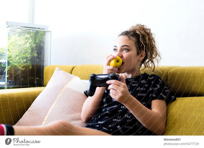 Porträt des Mädchens sitzt auf der Couch zu Hause essen einen Apfel, während das Spielen mit Spielen Konsole spielen Portrait Porträts Portraits Äpfel Aepfel