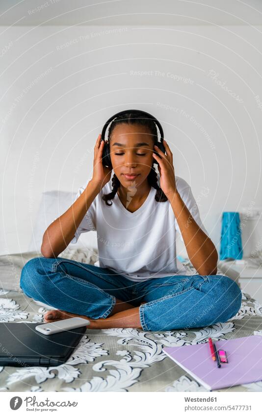 Teenager-Mädchen mit gekreuzten Beinen hört Musik, während sie zu Hause sitzt Farbaufnahme Farbe Farbfoto Farbphoto Innenaufnahme Innenaufnahmen innen drinnen