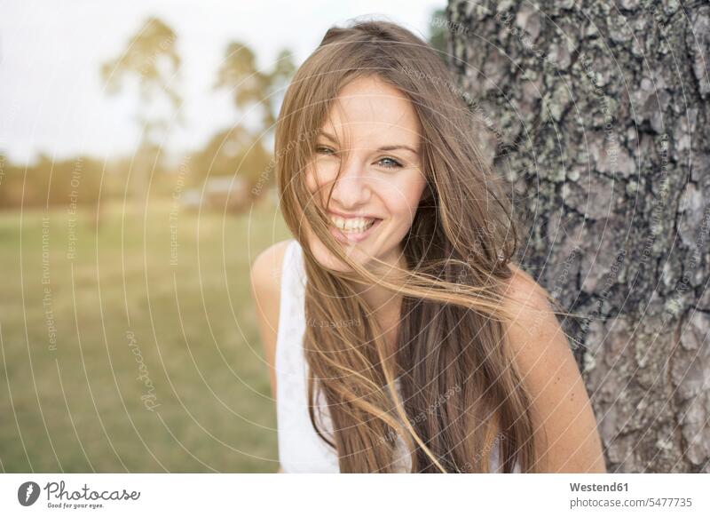 Porträt einer lachenden jungen Frau, die sich gegen einen Baumstamm lehnt Portrait Porträts Portraits weiblich Frauen Stamm Stämme Baumstämme anlehnen angelehnt