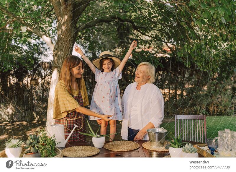 Fröhliches Mädchen mit erhobenen Armen steht mit Mutter und Großmutter an Baum im Hof Farbaufnahme Farbe Farbfoto Farbphoto Spanien Freizeitbeschäftigung Muße