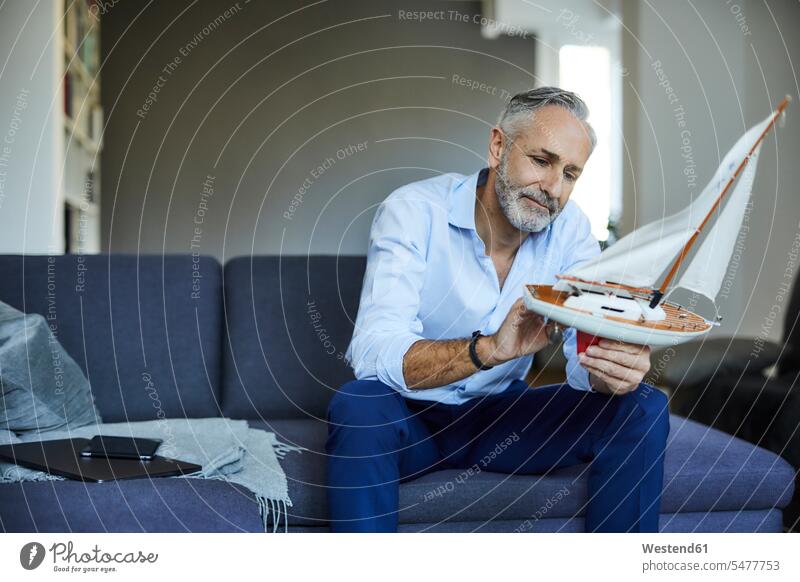 Älterer Mann hält Modell-Segelboot zu Hause Leute Menschen People Person Personen Alleinstehende Alleinstehender Singles Unverheiratete Unverheirateter Hemden