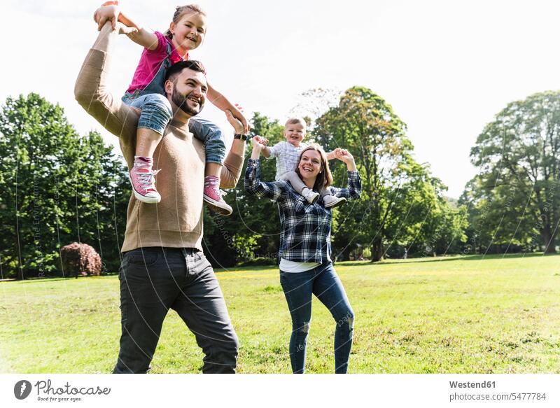 Glückliche Eltern tragen Kinder auf den Schultern in einem Park Familie Familien Huckepack transportieren Parkanlagen Parks glücklich glücklich sein