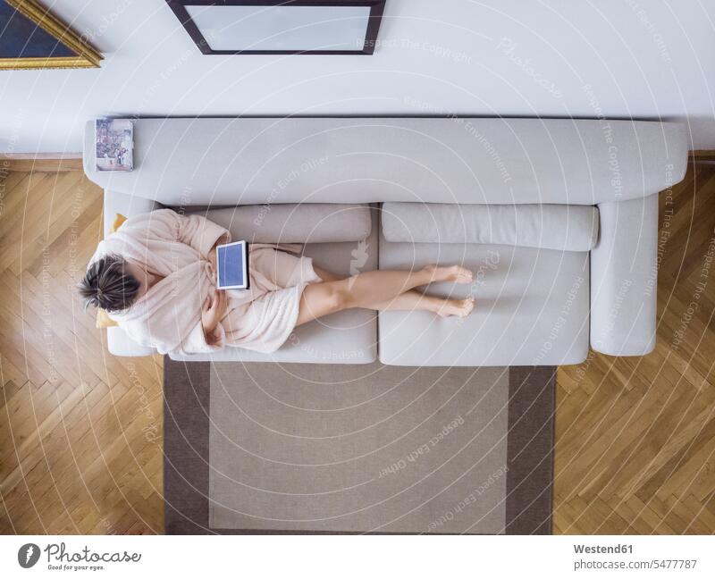 Reife Frau im Bademantel sitzt auf der Couch zu Hause mit digitalen Tablette Tablet Computer Tablet-PC Tablet PC iPad Tablet-Computer Zuhause daheim Bademäntel
