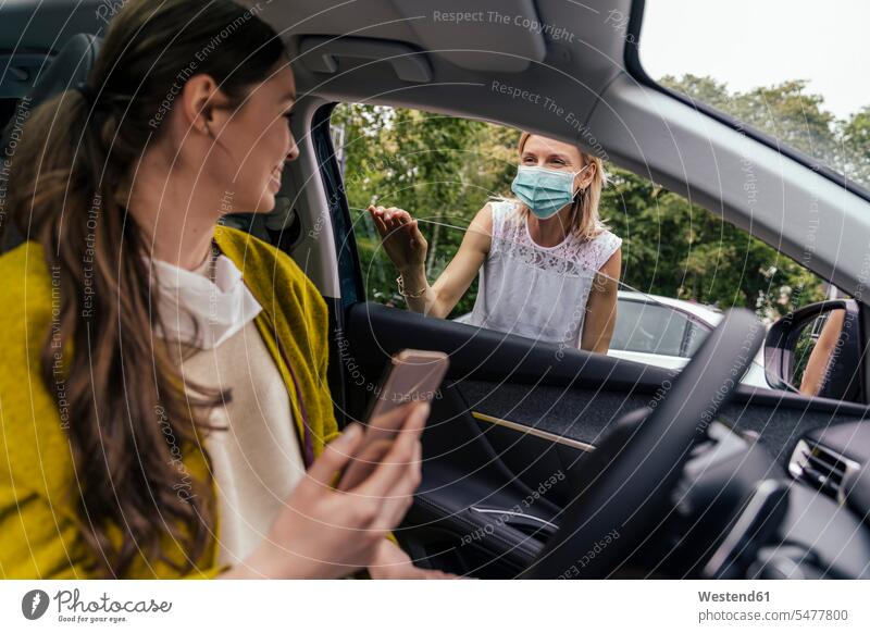 Frau mit Schutzmaske spricht durch Autofenster mit Frau ohne Maske KFZ Verkehrsmittel Automobil Autos PKW PKWs Wagen Telekommunikation Handies Handys