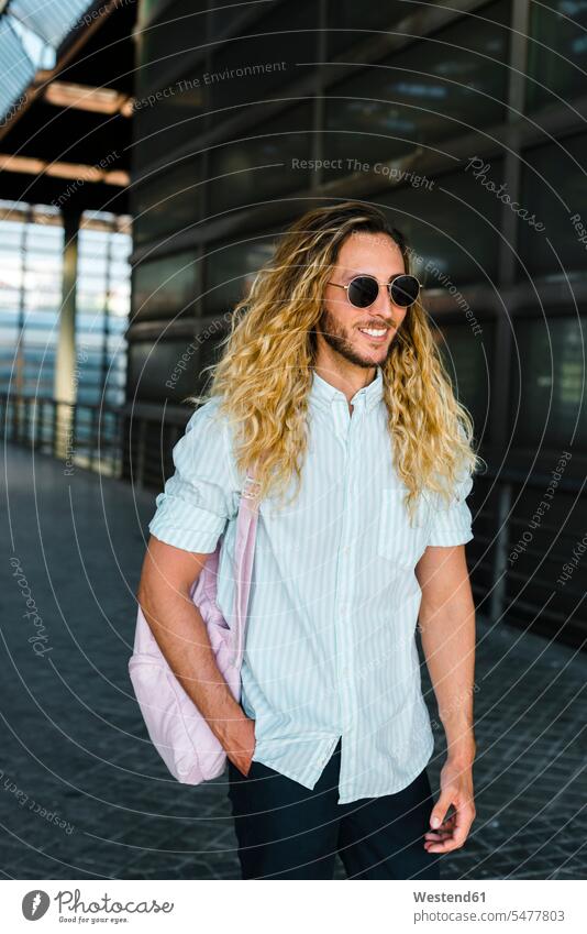 Lächelnder männlicher Hipster geht am Bahnhof Farbaufnahme Farbe Farbfoto Farbphoto Außenaufnahme außen draußen im Freien Tag Tageslichtaufnahme