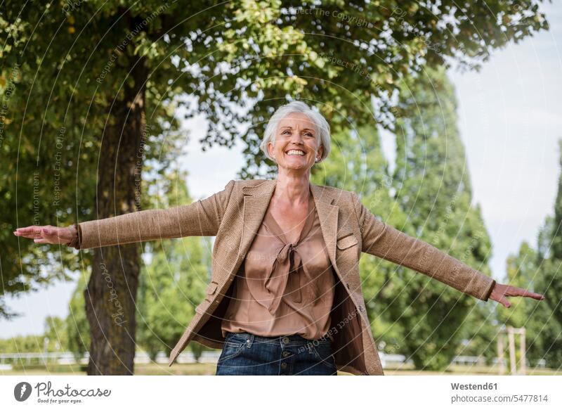 Glückliche ältere Frau mit ausgestreckten Armen in einem Park Seniorin Seniorinnen alt weiblich Frauen Parkanlagen Parks glücklich glücklich sein glücklichsein