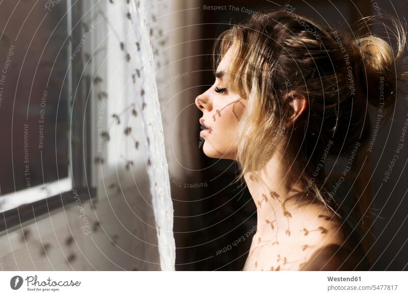 Verführerische Frau mit Schatten eines Vorhangs am Fenster zu Hause Farbaufnahme Farbe Farbfoto Farbphoto Innenaufnahme Innenaufnahmen innen drinnen Tag