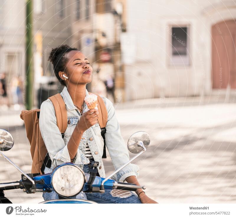 Glückliche junge Frau mit Motorroller beim Eisessen in der Stadt, Lissabon, Portugal Leute Menschen People Person Personen Afrikanisch Afrikanische Abstammung