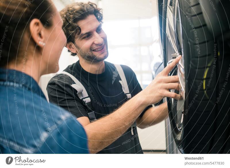 Lächelnder Automechaniker und Kunde betrachtet Reifen in der Werkstatt Job Berufe Berufstätigkeit Beschäftigung Jobs Gewerbe industriell Industrien Monteur KFZ