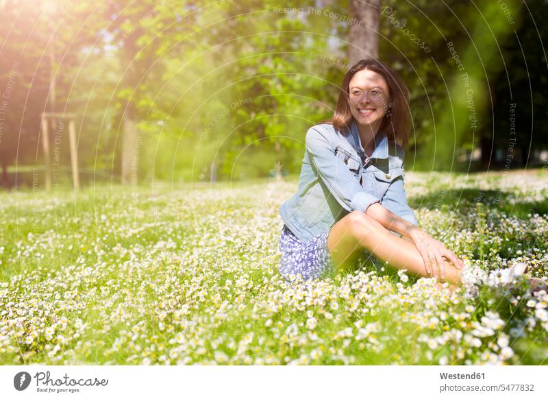 Lächelnde junge Frau sitzt in einem Park lächeln Parkanlagen Parks weiblich Frauen sitzen sitzend Erwachsener erwachsen Mensch Menschen Leute People Personen