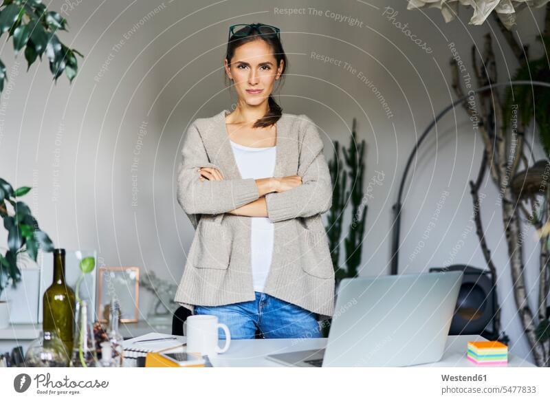 Selbstbewusste junge Frau steht am Schreibtisch mit Laptop Zuversicht stehen Tisch Erwachsener Mensch Computer Technologie Selbstbewusstsein Kaffeetasse
