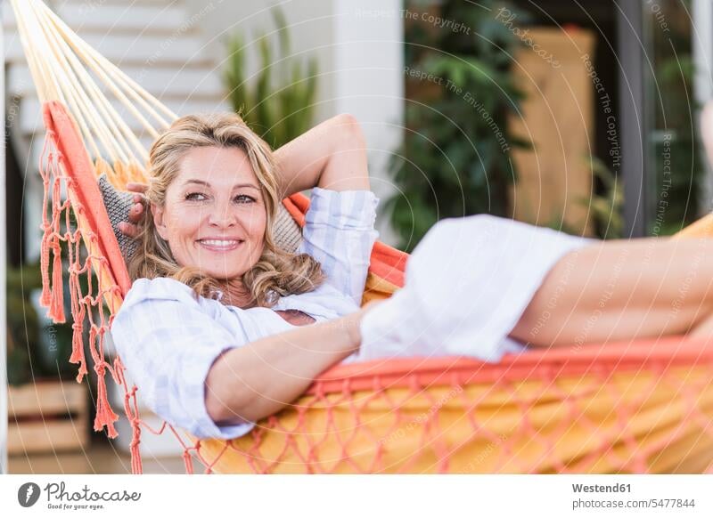 Porträt einer lächelnden reifen Frau, die sich in der Hängematte auf der Terrasse entspannt Hängematten entspannen relaxen freuen Glück glücklich sein