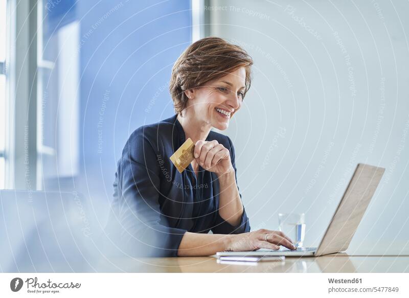 Lächelnde Geschäftsfrau mit Kreditkarte und Laptop am Schreibtisch im Büro Job Berufe Berufstätigkeit Beschäftigung Jobs geschäftlich Geschäftsleben