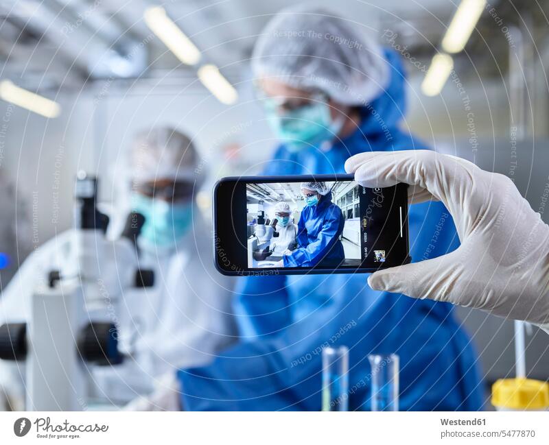 Hand hält Smartphone, fotografiert Chemiker, arbeitet im Industrielabor fotografieren Chemikanten iPhone Smartphones Chemielabor chemisches Labor Schutzanzug