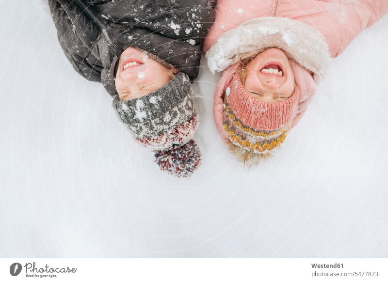 Porträt von zwei Geschwistern auf Schnee liegend Jahreszeiten winterlich Winterzeit freuen Frohsinn Fröhlichkeit Heiterkeit Glück glücklich sein glücklichsein