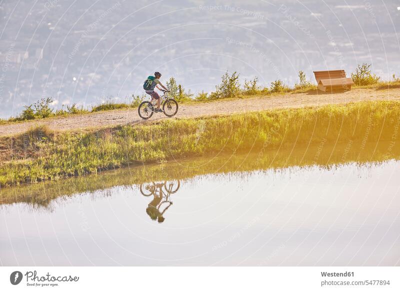 Österreich, Tirol, Mountainbikerin am See im Abendlicht Abenteuer abenteuerlich radfahren fahrradfahren radeln abends Mountainbiking mountainbiken MTB fahrend