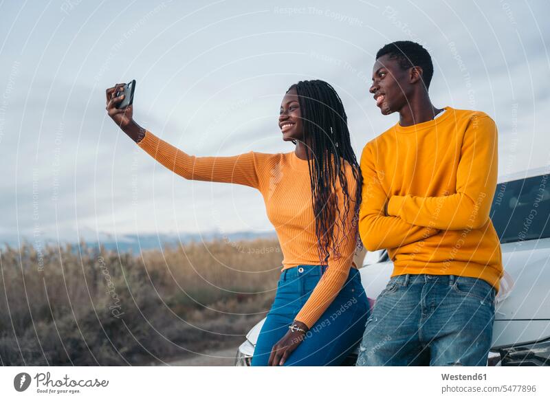 Lächelndes Paar, das ein Selfie macht, während es sich an die Wand lehnt Farbaufnahme Farbe Farbfoto Farbphoto Außenaufnahme außen draußen im Freien Tag