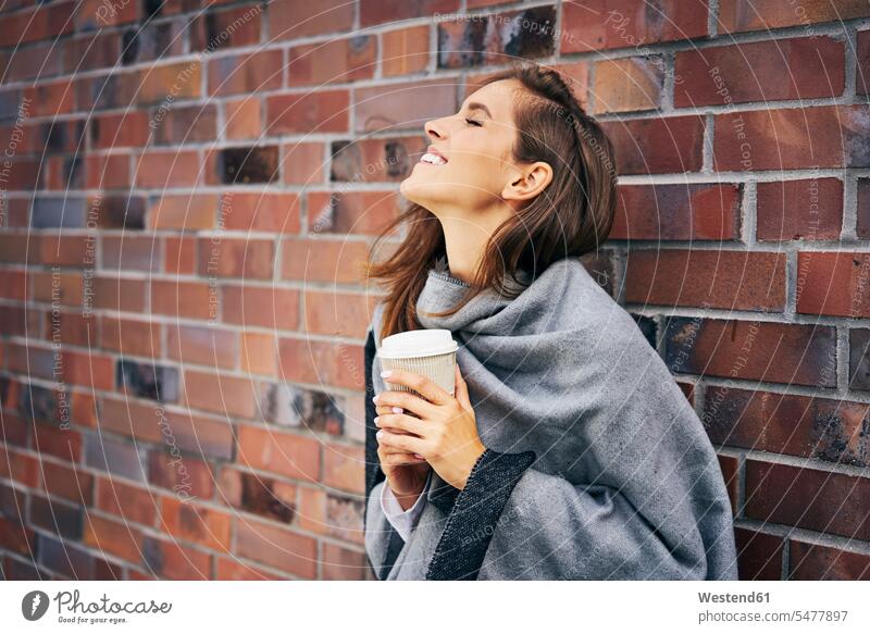 Glückliche Frau mit Kaffee vor Backsteinmauer weiblich Frauen glücklich glücklich sein glücklichsein Backsteinwand Backsteinmauern Coffee to go zum mitnehmen