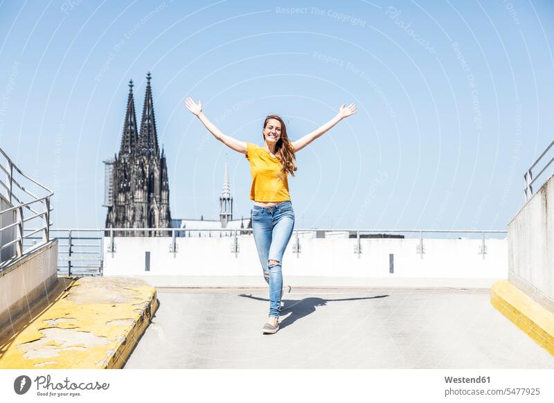 Deutschland, Köln, glückliche Frau auf der Rampe der Parkebene mit dem Kölner Dom im Hintergrund weiblich Frauen Glück glücklich sein glücklichsein Parkdeck