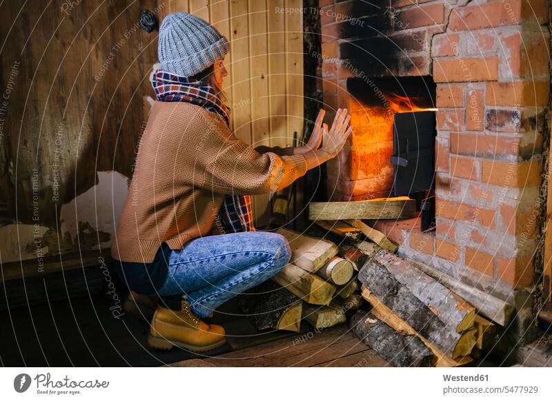 Frau kauert vor dem Kamin und wärmt ihre Hände Öfen Schals Jahreszeiten winterlich Winterzeit daheim zu Hause warm Flammen Muße behaglich Gemütlichkeit