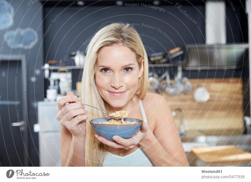 Porträt einer lächelnden blonden Frau in der Küche beim Essen von Getreide Küchen essen essend Portrait Porträts Portraits weiblich Frauen blonde Haare
