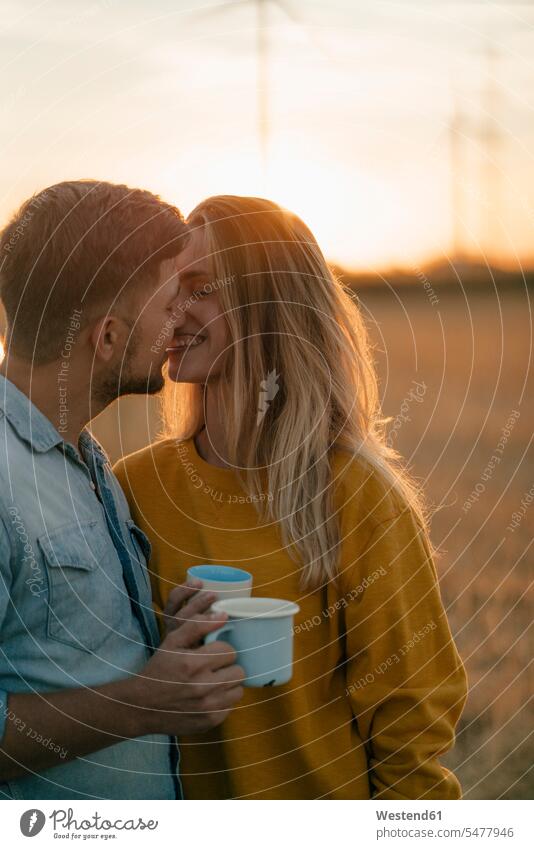Glückliches junges Paar hält Tassen küssen in der ländlichen Landschaft Becher Landschaften auf dem Land auf dem Lande glücklich glücklich sein glücklichsein