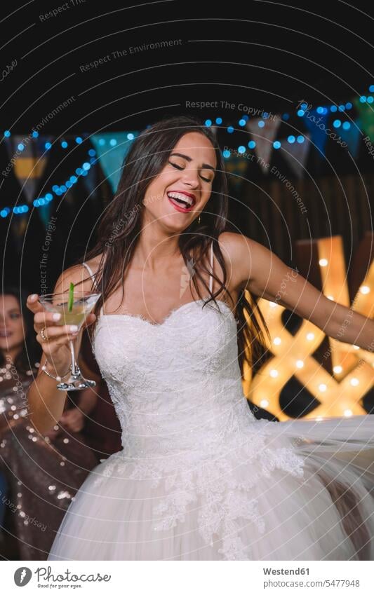 Glückliche Braut lacht und tanzt, während sie auf einer Nachtparty im Freien einen Cocktail trinkt Spaß Spass Späße spassig Spässe spaßig Bräute lachen Party