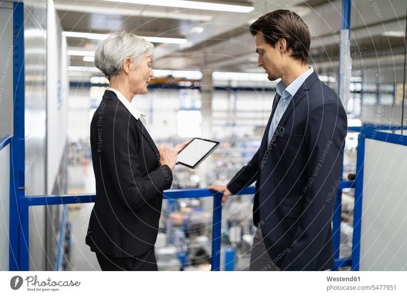 Geschäftsmann und ältere Geschäftsfrau mit Tablet im Gespräch in einer Fabrik sprechen reden Tablet Computer Tablet-PC Tablet PC iPad Tablet-Computer