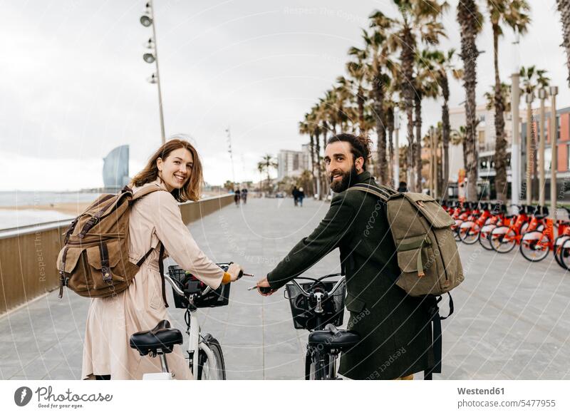 Lächelndes Paar mit E-Bikes auf der Strandpromenade Strandpromenaden eBikes Elektrofahrrad Elektrorad lächeln Pärchen Paare Partnerschaft Fahrrad Fahrräder
