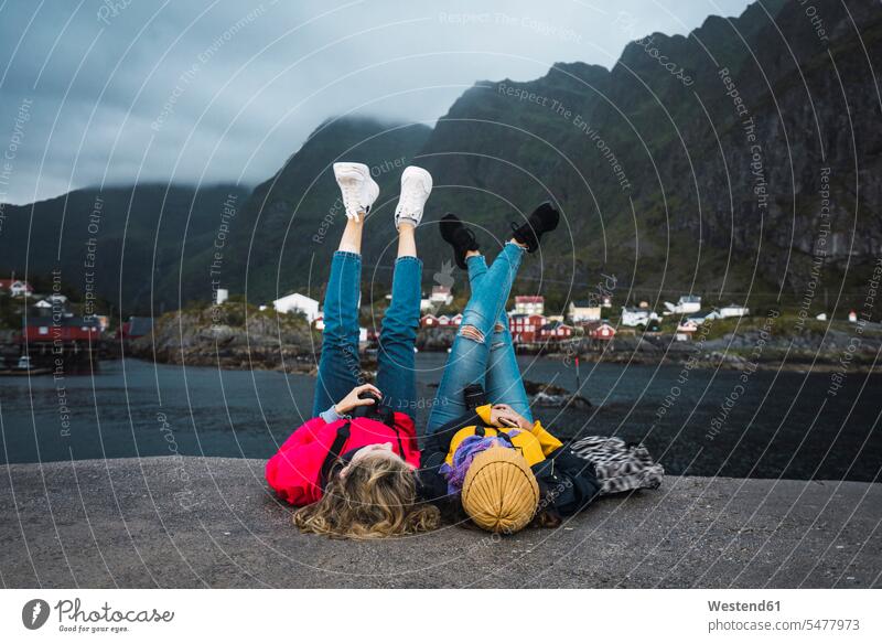 Norwegen, Lofoten, zwei junge Frauen liegen auf einem Pier an der Küste weiblich Landungssteg Piers Kueste Kuesten Küsten liegend liegt Erwachsener erwachsen