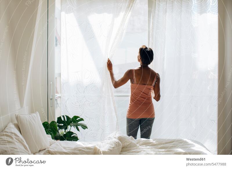 Frau, die zu Hause am Fenster im Schlafzimmer steht Leute Menschen People Person Personen Alleinstehende Alleinstehender Singles Unverheiratete Unverheirateter