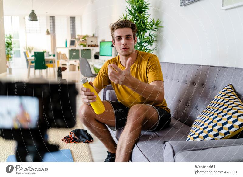Fitnesstrainer Live-Streaming-Fitness-Sitzung, während er zu Hause auf dem Sofa sitzt Farbaufnahme Farbe Farbfoto Farbphoto Innenaufnahme Innenaufnahmen innen