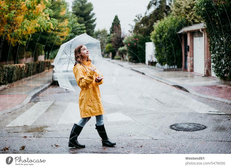 Lächelndes Mädchen in Regenmantel mit Regenschirm beim Spaziergang auf der Straße in der Stadt Farbaufnahme Farbe Farbfoto Farbphoto Tag Tageslichtaufnahme